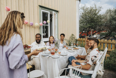 Woman serving food to male and female friends during dinner party at cafe