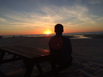 Rear view of man sitting in water at sunset