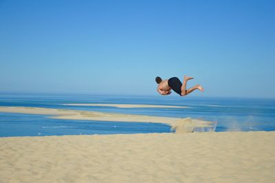 Rear view of woman jumping at beach against clear blue sky