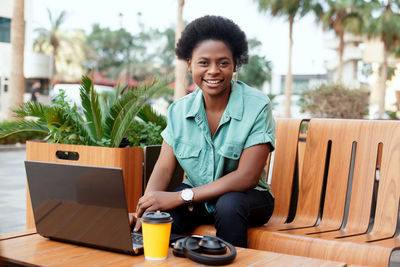 Portrait of smiling young woman with laptop sitting at outdoor cafe