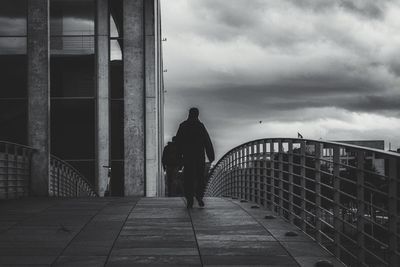 Rear view of man walking on railing against sky
