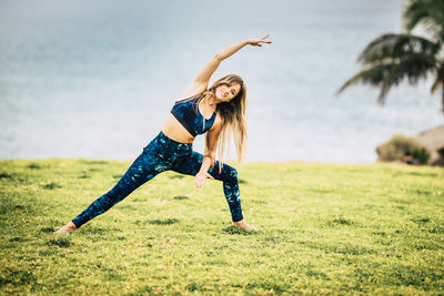 Full length of smiling woman exercising on grass