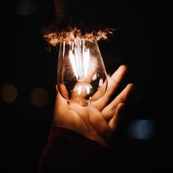 Close-up of woman hand by illuminated light bulb at night