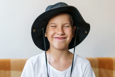 Cheerful school-age boy in white t-shirt and black hat sits on the couch