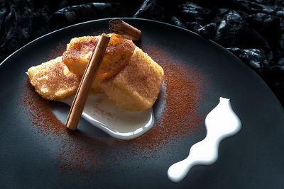 Traditional spanish dessert of fried milk with cinnamon and condensed milk on black plate