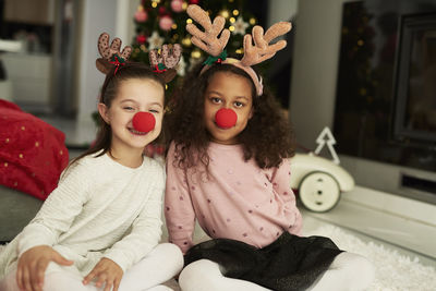 Portrait of girls wearing christmas props while sitting on rug at home