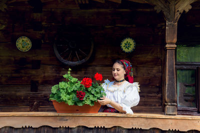 Smiling woman touching potted plant in balcony