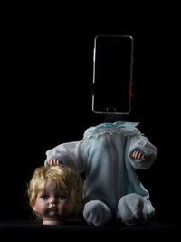 Close-up of broken doll with mobile phone against black background