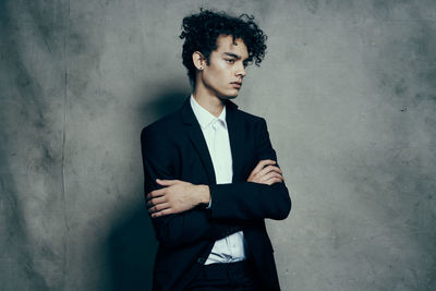 Young man looking away while standing against wall