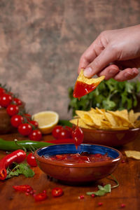 Cropped hand dipping nachos in sauce on table