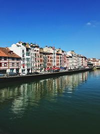 Buildings by river against blue sky