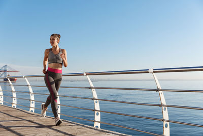 Full length of woman running by railing against sea