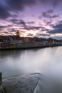 River by buildings in city against sky during sunset