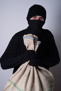 Portrait of man in costume holding sack while standing against wall