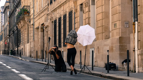 Man holding umbrella on road by buildings in city