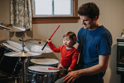 Father looking at cute baby son making face while playing drums