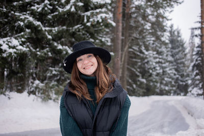 Portrait of smiling woman wearing hat standing against snow covered trees