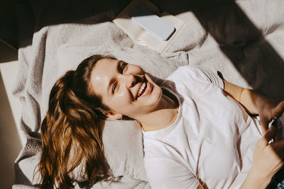 Portrait of cheerful young woman lying on bed at home