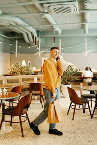 A young man in casual clothes with bags in his hands after shopping stands alone and talks in a cafe