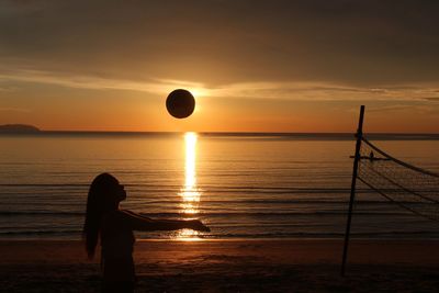 Silhouette woman playing volleyball at beach against sky during sunset