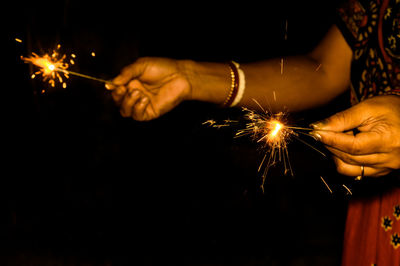 Midsection of woman holding sparklers standing against black background