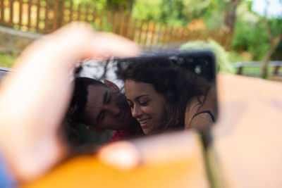 Couple embracing reflecting in smart phone outdoors