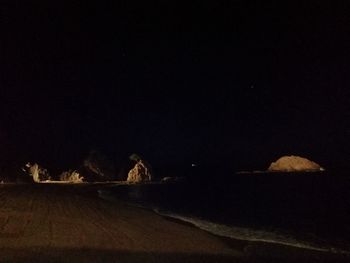 Illuminated road on silhouette landscape against sky at night