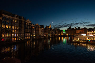 River by illuminated buildings against sky at dusk