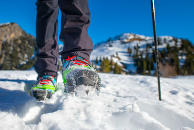 Low section of man walking on snow covered land against clear blue sky