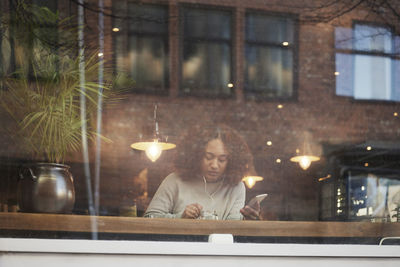 Young woman using cell phone and eating in cafe