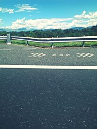 Road passing through field against cloudy sky