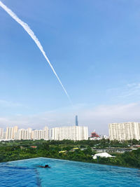 Vapor trails over buildings in city against blue sky
