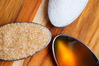 Spoons with raw honey, brown and white sugar on wooden table