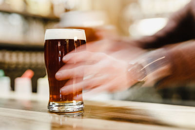 Close-up of hand holding beer glass on table