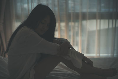 Side view of woman sitting on bed at home