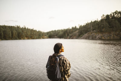 Rear view of woman with backpack standing against lake in forest