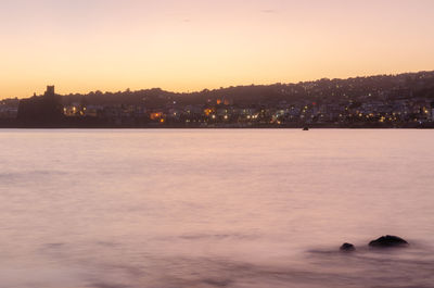 Silhouette buildings by sea against sky during sunset