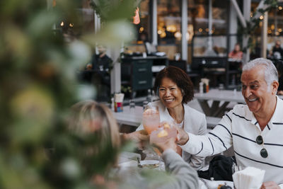 Smiling senior man toasting drinks with male and female friends at restaurant