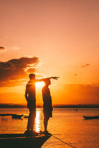 Silhouette of two man standing at beach against sky during sunset