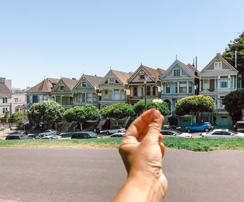 Hand holding camomile flower  against painted sisters buildings in san francisco city