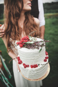 Midsection of couple holding wedding cake at farm