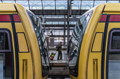 Side view of man walking with luggage at railroad station seen through trains