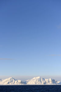 Scenic view of snowcapped mountains against clear blue sky during winter