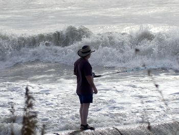 Rear view of man standing  at the ocean fishing