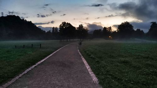 Road amidst field against sky during sunset