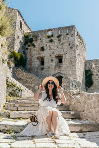 Front view of beautiful woman sitting on stone stairs in medieval fortress klis in split, croatia