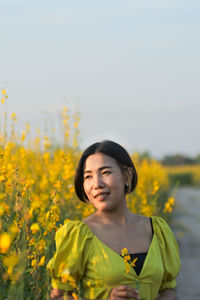 Portrait of beautiful woman standing on field against yellow sky