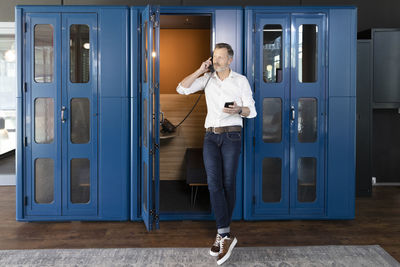 Full length of man holding camera while standing against blue wall