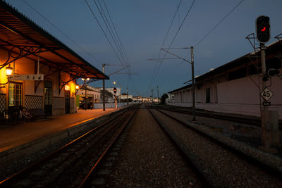 Railroad tracks in illuminated station against sky