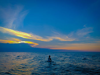 Silhouette man in sea against sky during sunset